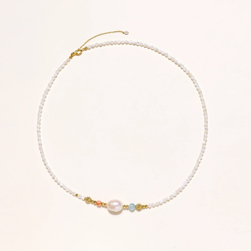 Beaded necklace with small white moonstone beads, central baroque freshwater pearl, coral and blue stone accents, gold floral spacers.