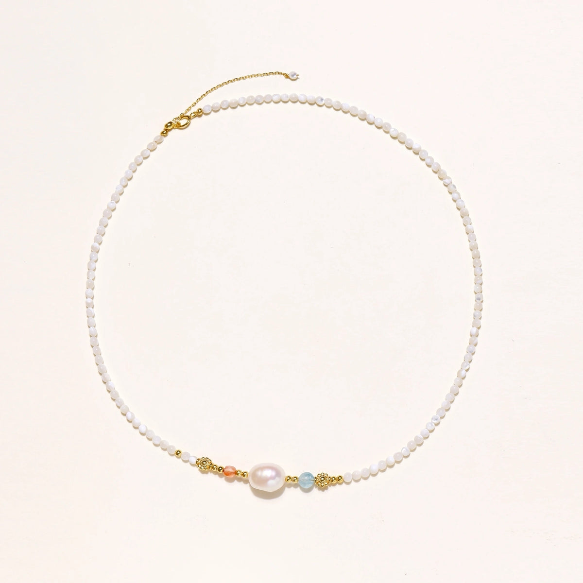 Beaded necklace with small white moonstone beads, central baroque freshwater pearl, coral and blue stone accents, gold floral spacers.